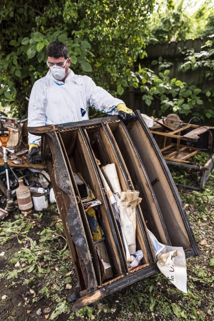 volunteer in PPE practices flood cleanup safety as they remove debris from home